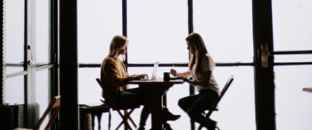 Two colleagues having a discussion whilst sat down at a table.